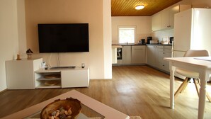 Una cocina moderna con televisor de pantalla plana, piso de madera y armarios blancos.