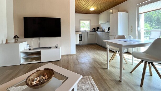Una cocina moderna con una televisión de pantalla plana, suelo de madera y una zona de comedor con mesa y sillas.