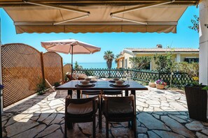 Eine Terrassensitzgruppe im Freien mit Tisch, Sonnenschirm und Blick aufs Meer.
