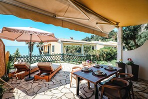 Eine Terrasse mit Gartenmöbeln, einem Esstisch und Blick aufs Meer.