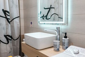 Ein Badezimmer mit einem weißen Waschbecken, einem Spiegel mit schwarzem Rahmen und zwei gemusterten Tassen auf der Ablagefläche.