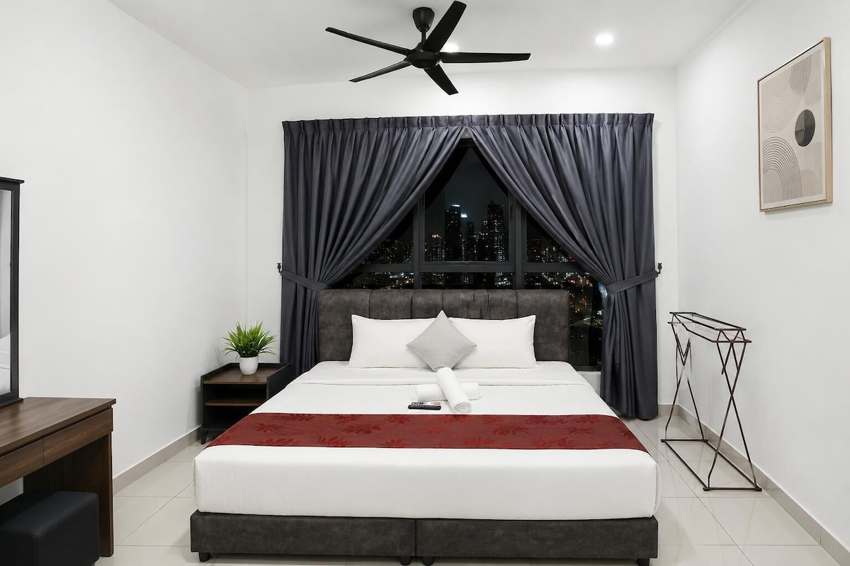A modern bedroom with a bed, a ceiling fan, a nightstand with a plant, and a view of the city at night.