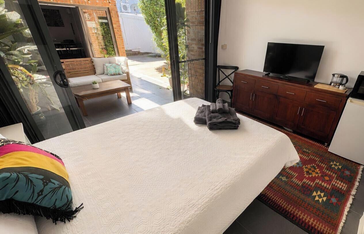 A bedroom with a bed, a TV, a wooden cabinet, and a view of the outside.