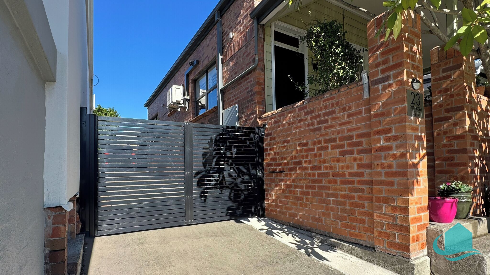 A gated entrance with a metal gate, a brick wall, and a potted plant.