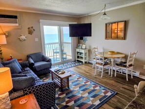 Un salon comprenant un canapé, un fauteuil, une table basse et un téléviseur fixé au mur.