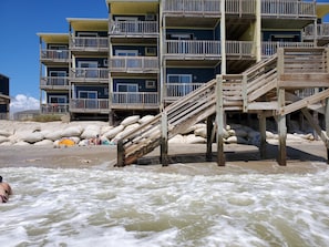 Un immeuble à plusieurs étages doté de balcons, d’escaliers en bois et d’une zone de plage de sable.