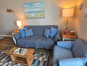 Ein Wohnzimmer mit einem gemusterten Sofa, einem kleineren Couchtisch, einem Couchtisch und einem Bild an der Wand sowie einer Lampe.