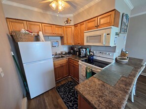 A kitchen with wooden cabinets, a white refrigerator, a microwave, a stove, and a granite countertop. - Ocean Front Condo 376 directly on the beach (North Topsail Beach)