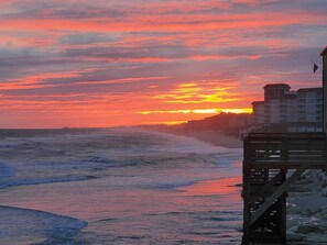 A coastal sunset with waves, a wooden pier, and buildings in the background. - Ocean Front Condo 376 directly on the beach (North Topsail Beach)