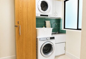 A compact laundry room with a washing machine, dryer, and stacked drying rack. - Artistic Parkside Retreat with Deck (South Fremantle)