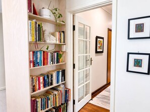 A hallway with a bookshelf, a door with frosted glass panels, and framed artwork on the wall. - Artistic Parkside Retreat with Deck (South Fremantle)