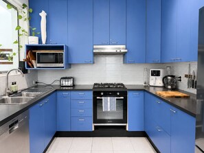 A modern kitchen with blue cabinets, stainless steel appliances, and a tiled backsplash. - Artistic Parkside Retreat with Deck (South Fremantle)