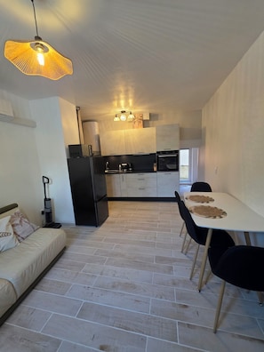 A compact kitchen with a dining area, a sofa, and a ceiling light fixture. - Le Cocon Provençal balneo Spa. Apartment at the gateway to the Luberon, a Zen interlude (Cavaillon)
