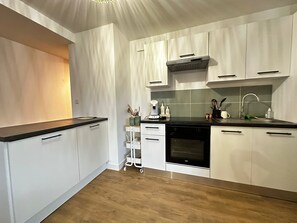 Moderni keittiö, jossa on valkoiset kaapit, musta työtaso ja sisäänrakennettu uuni.