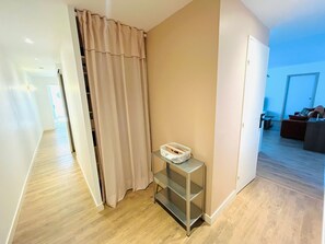 A hallway with a sliding door, a small metal shelf with a basket, and a view into a living area with a couch and a coffee table.
