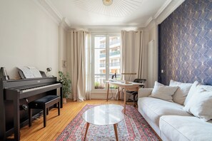 Ein Wohnzimmer mit Klavier, einer Couch, einem Couchtisch und Blick auf einen Balkon.