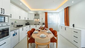 Eine moderne Küche mit weißen Schränken, einem Esstisch mit orangefarbenen Stühlen und einem eingebauten Backofen.