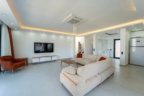 A modern living room with a sectional sofa, a TV, a coffee table, and a dining area with a refrigerator. - Just 500 Meters to the Beach: Sea View, Private Pool, 10-Guest Villa in Kışla (Antalya)