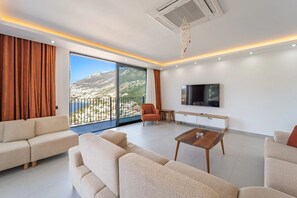 A modern living room with a sofa set, a coffee table, a TV, and a balcony with a mountain view. - Just 500 Meters to the Beach: Sea View, Private Pool, 10-Guest Villa in Kışla (Antalya)