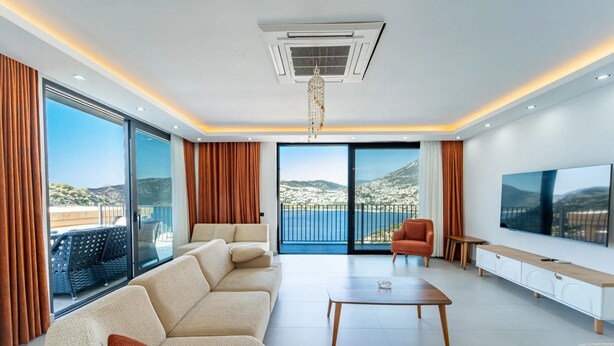 Ein modernes Wohnzimmer mit einer Sofagarnitur, einem Couchtisch, einem Fernseher und einem Balkon mit Meerblick.