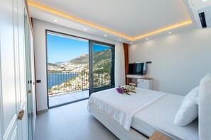 A bedroom with a bed, a TV, a balcony with a city view, and a door. - Just 500 Meters to the Beach: Sea View, Private Pool, 10-Guest Villa in Kışla (Antalya)