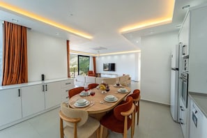 A modern dining area with a round table, chairs, and a kitchen area with a refrigerator. - Just 500 Meters to the Beach: Sea View, Private Pool, 10-Guest Villa in Kışla (Antalya)