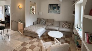 Ein Wohnzimmer mit einer Couch, einem runden Couchtisch, einem Sessel, einem Heizkörper und einem Bücherregal.