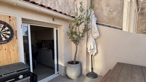 Eine Terrasse mit Grill, einem Holztisch, einem Kübelbaum und einem Dartboard.