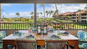 A dining area with a view of palm trees and a building in the background. - 2BR, 2BA Kaanapali Royal condo with pool, hot tub, kitchen, AC-Kaanapali Royal F302 (Lahaina)