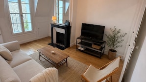 A living room with a sofa, a coffee table, a TV stand, a fireplace, and a plant. - COSY, FULLY-EQUIPPED APARTMENT (Paris)