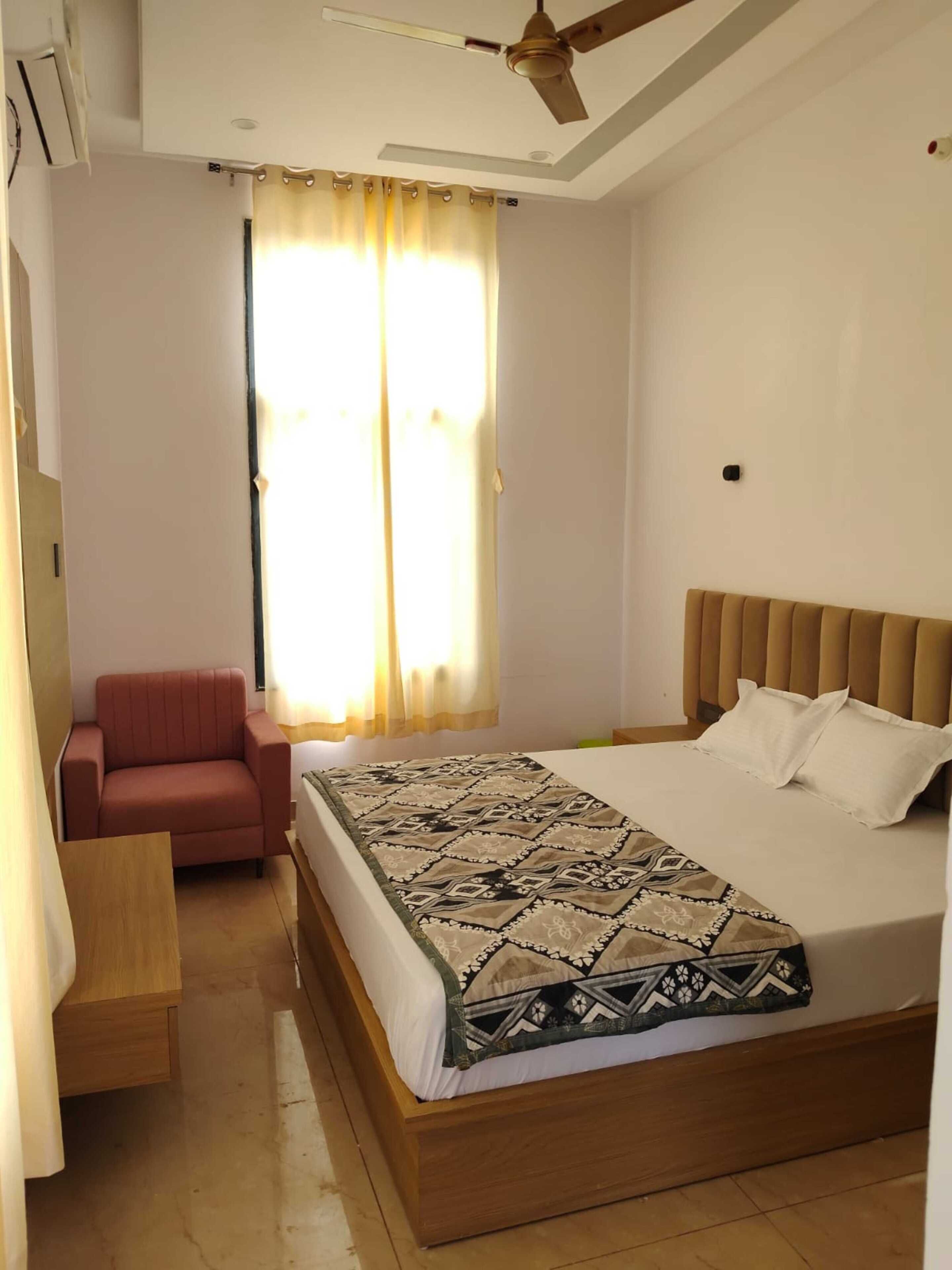 Quarto com cama, cadeira, ventilador de teto e janela com cortinas.