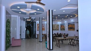 Een moderne hotellobby met een plafondventilator, inbouwverlichting, een receptiebalie en kunstwerken aan de muur.