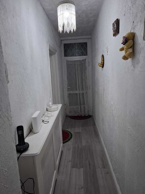 Ein schmaler Korridor mit einer weißen Tür, einer Chandelüster, einer weißen Theke mit einem Telefon und einem Teddybären an der Wand.