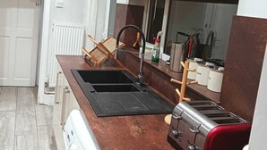 Een kleine keuken met een wasmachine, een inbouwoven, een broodrooster en een raam met een decoratief zonnescherm.