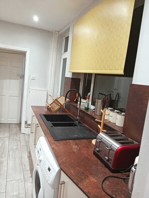Eine kompakte Küche mit Waschmaschine, Backofen, Toaster und einem Fenster mit gemustertem Rollo.