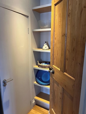 A narrow hallway with wooden shelving units, a door, and a small step leading to a lower level. - Apartment Sleeps 2 With Parking (Bridport)