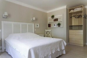 Ein Schlafzimmer mit Bett, Kleiderschrank, Nachttisch und Regalen an der Wand mit Gegenständen.