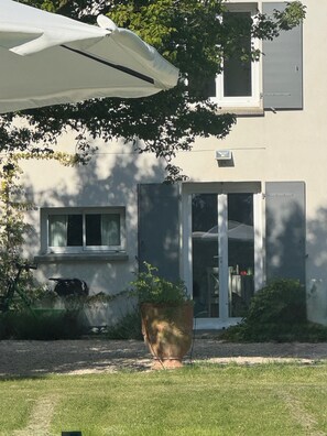 Et hus med et stort vindue, en dør og en potteplante i forgrunden.