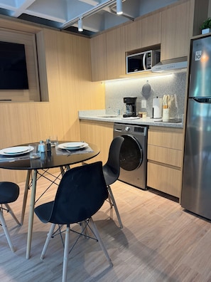 A modern kitchen with wooden cabinets, a built-in microwave, a coffee maker, a washing machine, and a refrigerator. - Modern 1BR in Juárez with fast WiFi, great natural light, a comfortable king bed, a fully equipped kitchen, and a luxury bathroom. Perfect for couples or solo travelers seeking comfort, style, and a prime location in Mexico City. (Cuauhtémoc)