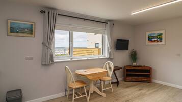Una habitación con una mesa y sillas de madera, una ventana con cortinas, un televisor y un armario pequeño.