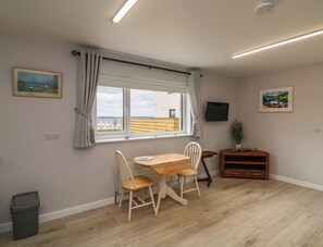 A room with a wooden table and chairs, a window with curtains, a television, and a small cabinet.