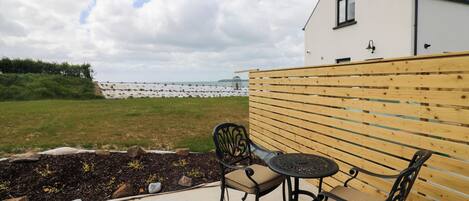 En terrasse med to stole og et bord, et træhegn og en bygning med et vindue.