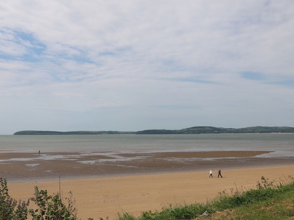 A beach with people walking, a calm sea, and distant hills.