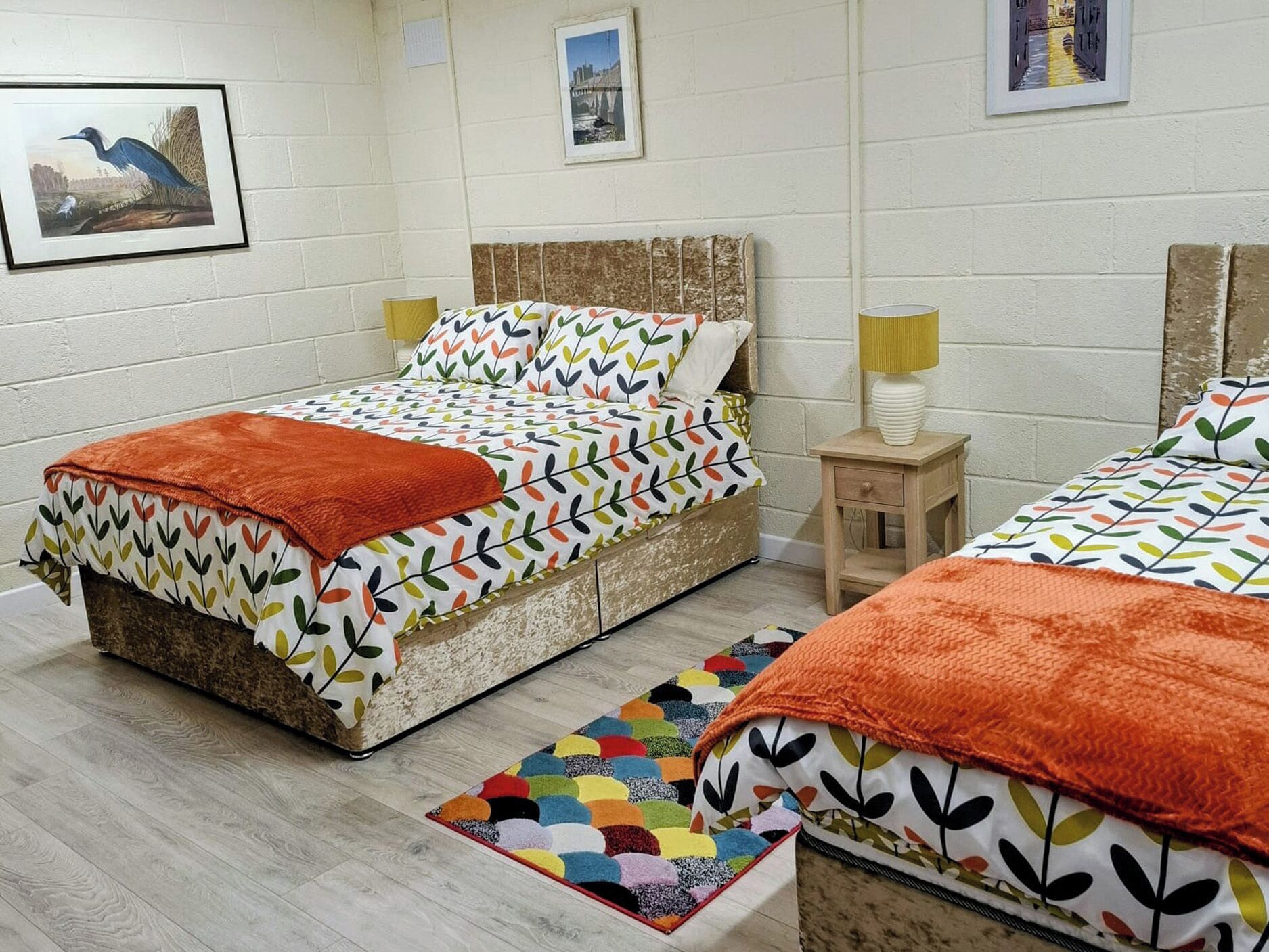 Una habitació amb dos llits, una catifes colorida i una taula petita amb una làmpada.