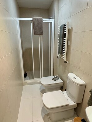 Ein Badezimmer mit Dusche, zwei Toiletten, einem Handtuchhalter und einer Heizung.