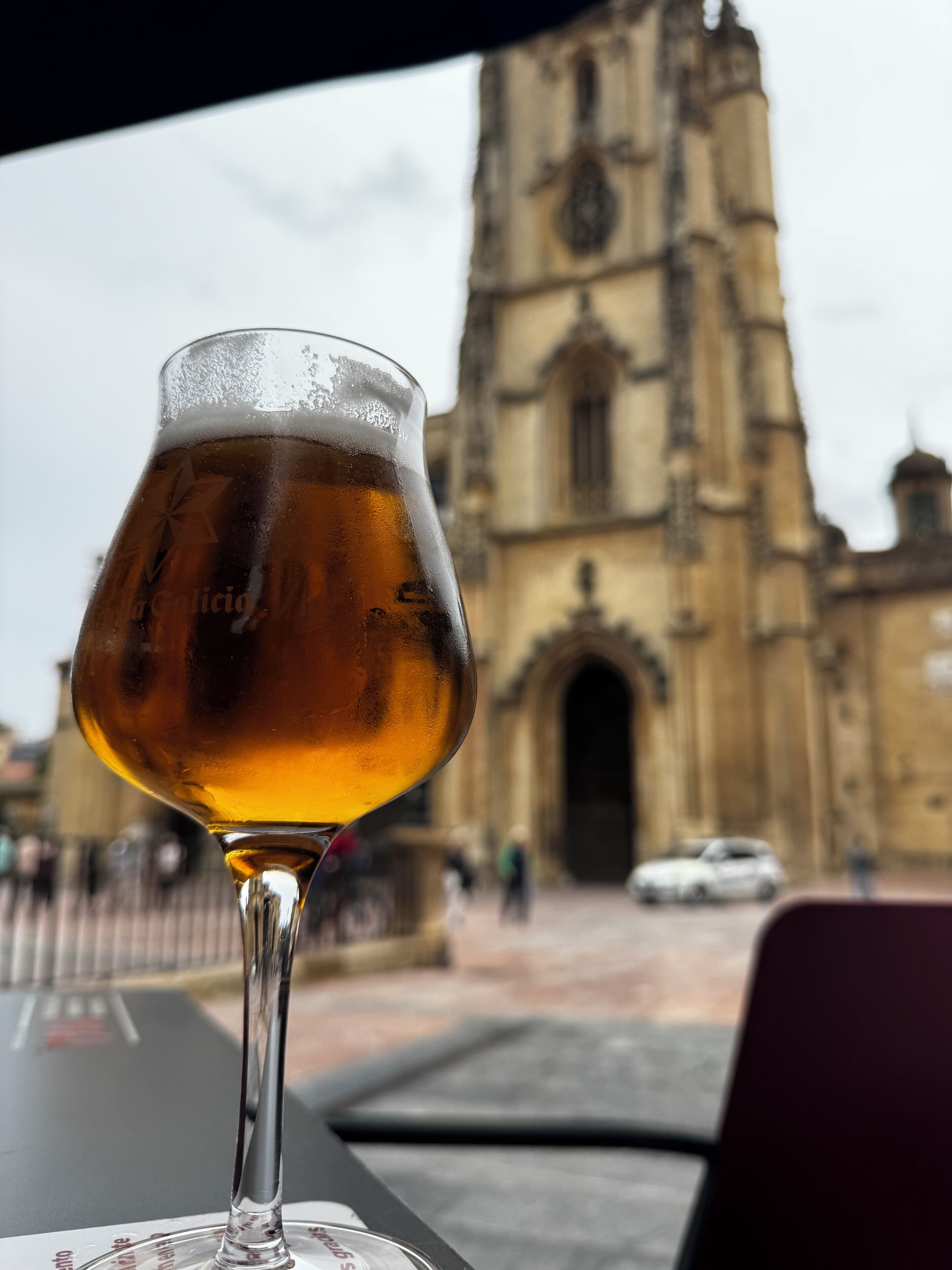 Un verre contenant un liquide ambré est posé sur une table, avec un bâtiment historique en arrière-plan.