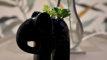 Eine schwarze, elefantenförmige Lampe mit einer kleinen Pflanze obenauf, platziert auf einer weißen Oberfläche, im Hintergrund ist ein Lampenschirm zu sehen.