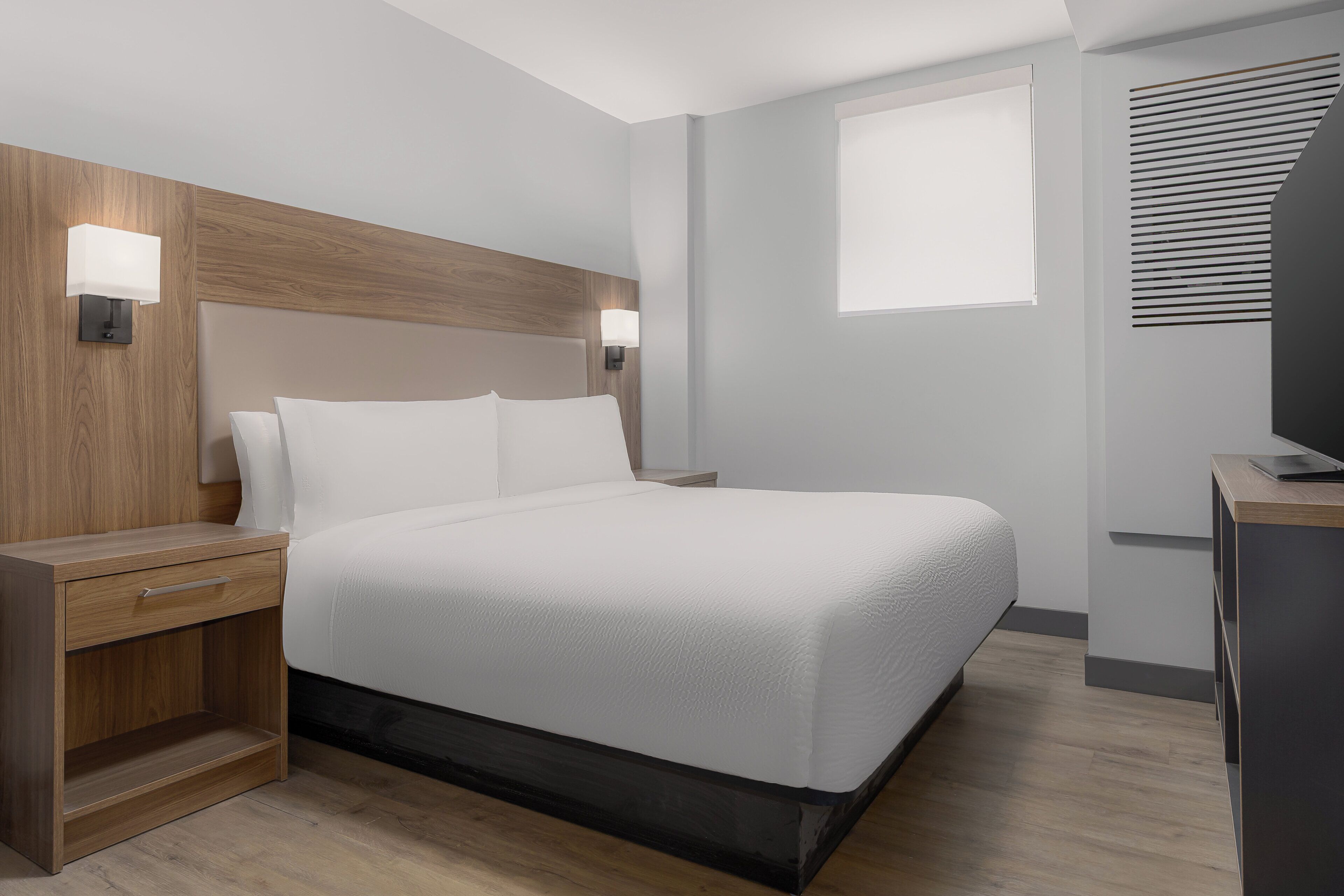 Una habitación de hotel moderna con una cama grande, mesitas de noche, un escritorio y una ventana con persianas.