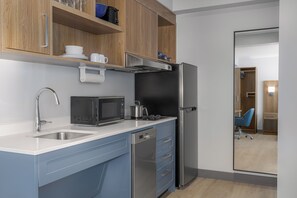 A compact kitchen with a microwave, stove, and refrigerator, wooden cabinets, and a blue countertop.