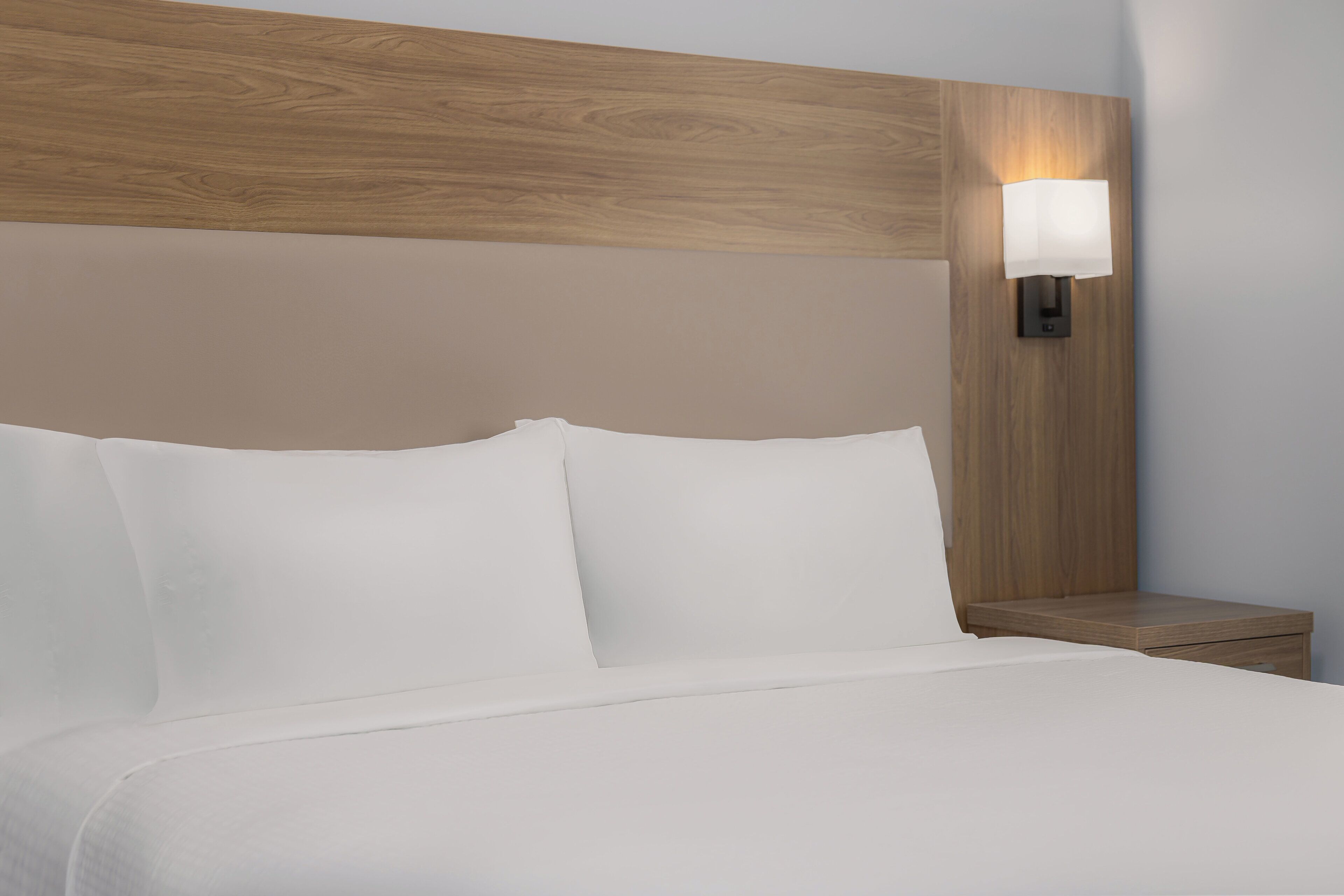 A neatly made bed with white linens and a wooden headboard.